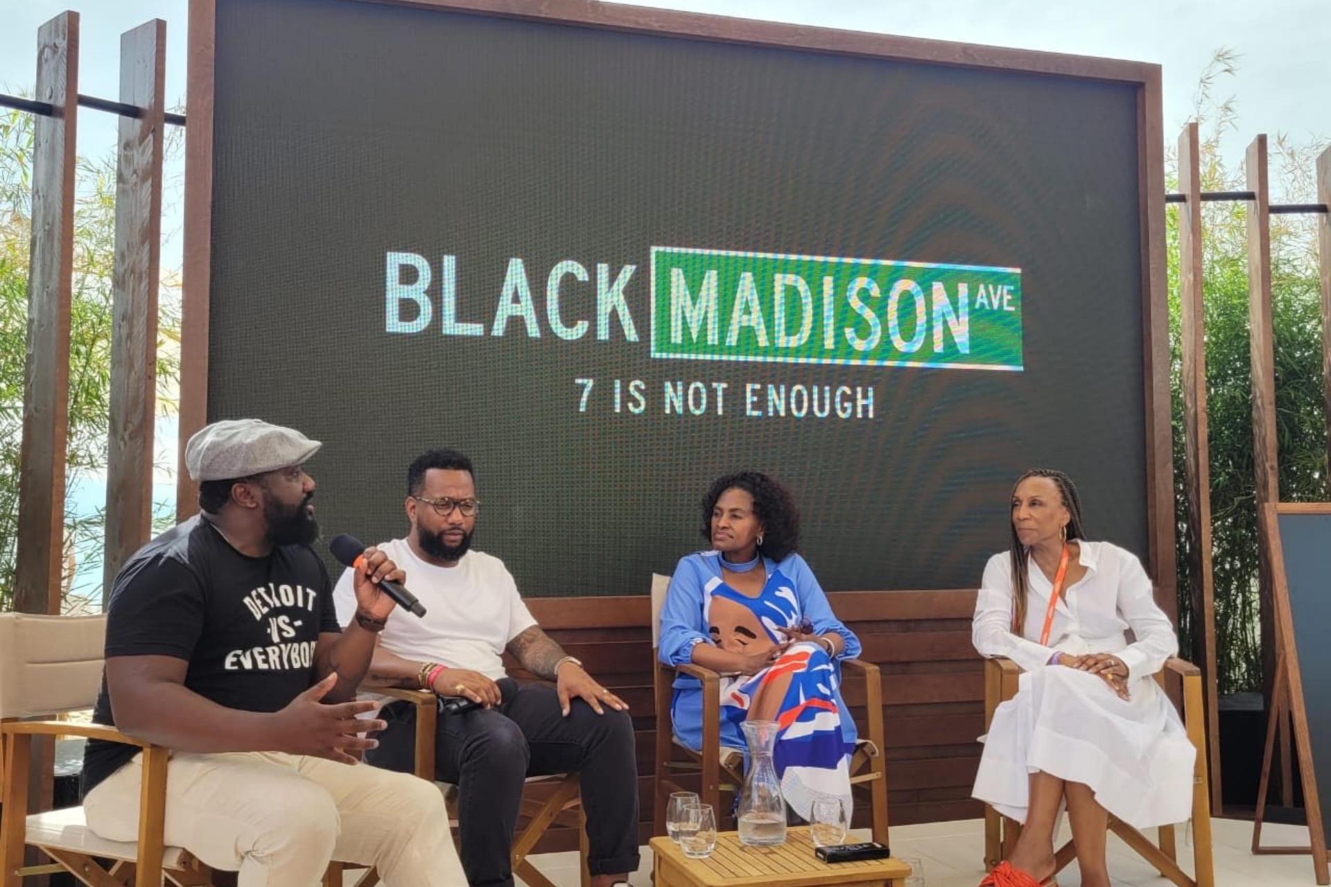 Four panelists onstage in front of a screen reading “Black Madison Ave: 7 Is Not Enough,” with a man wearing a “Detroit is Everybody” T-shirt speaking into the microphone.