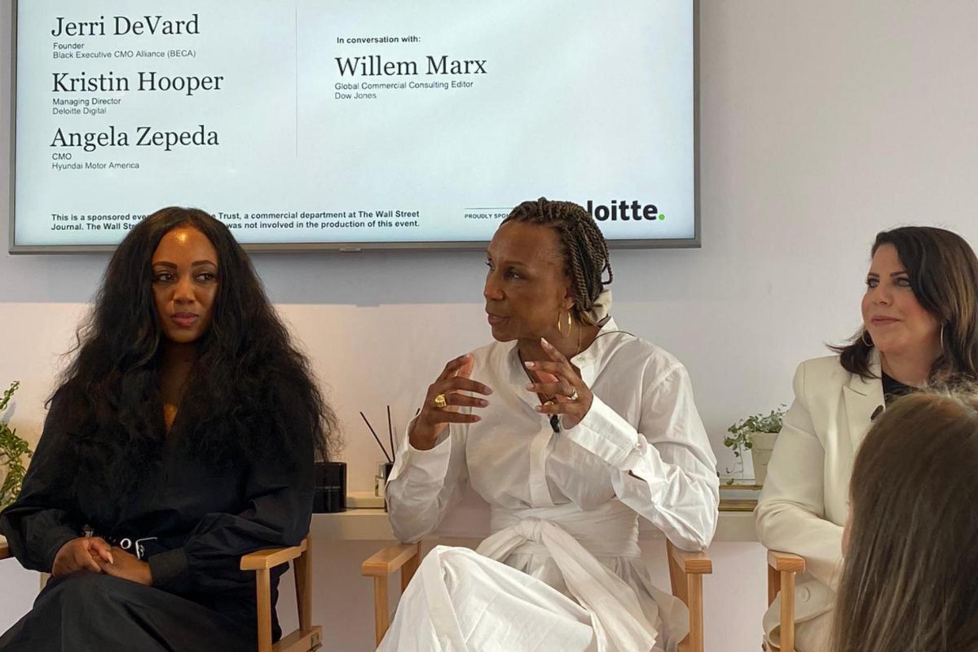 A closer view of the same panel, with a woman in a white belted dress (Jerri DeVard) speaking and gesturing as two other panelists look on.