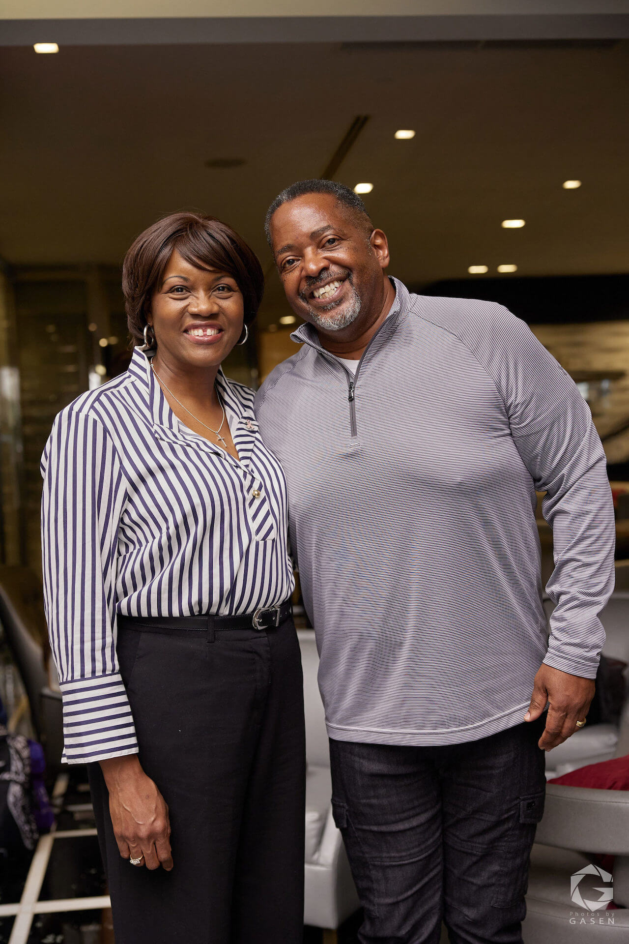 A woman in a striped shirt and a man in a gray pullover stand side by side, smiling for the camera.