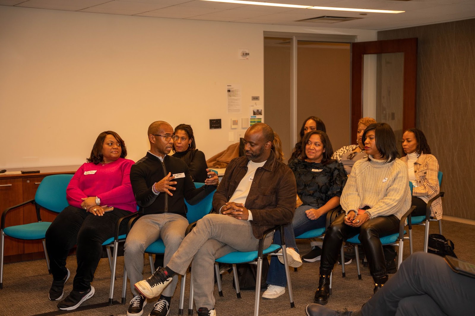 A group of attendees seated in a circle, one man gesturing as he speaks passionately, while others listen attentively in a professional setting.