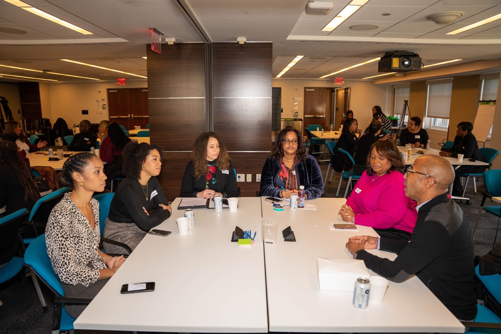 A group of six individuals sitting around a table in a conference room, engaged in discussion with notepads and drinks on the table.