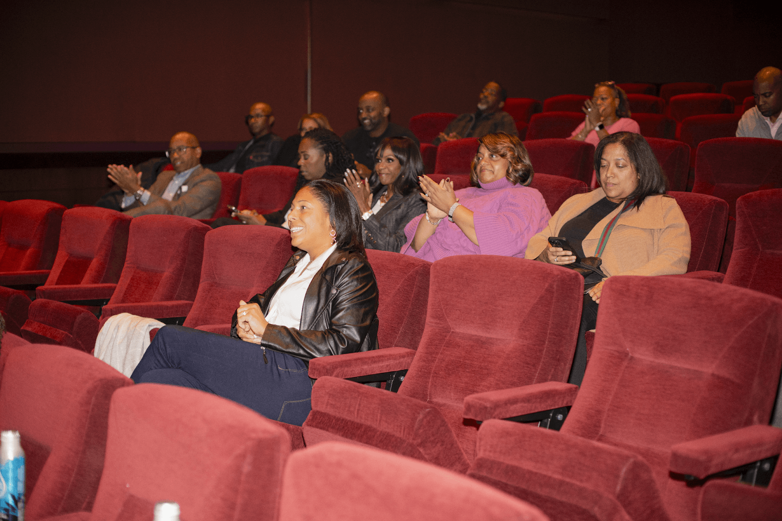 An audience seated in red theater chairs, attentively watching and applauding the panel discussion on stage.