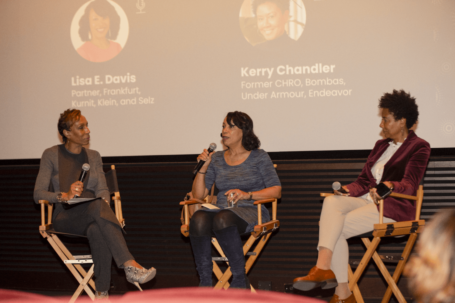 A closer view of the same panel discussion, with one panelist speaking while holding a microphone, and the others listening attentively.