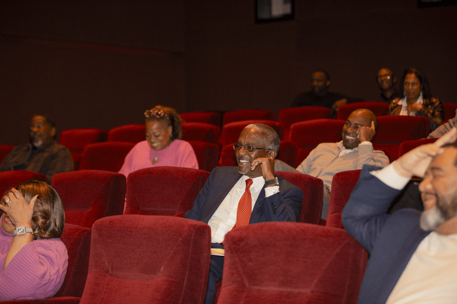 Audience members in red theater seats laughing and smiling during the event, showing engagement and enjoyment.