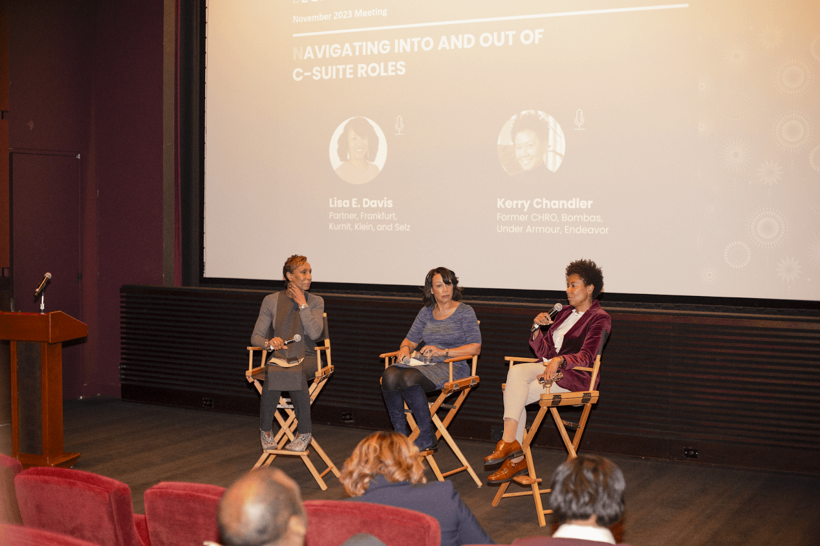 A wider view of the panel discussion, capturing the stage setup, screen presentation, and some audience members listening attentively.