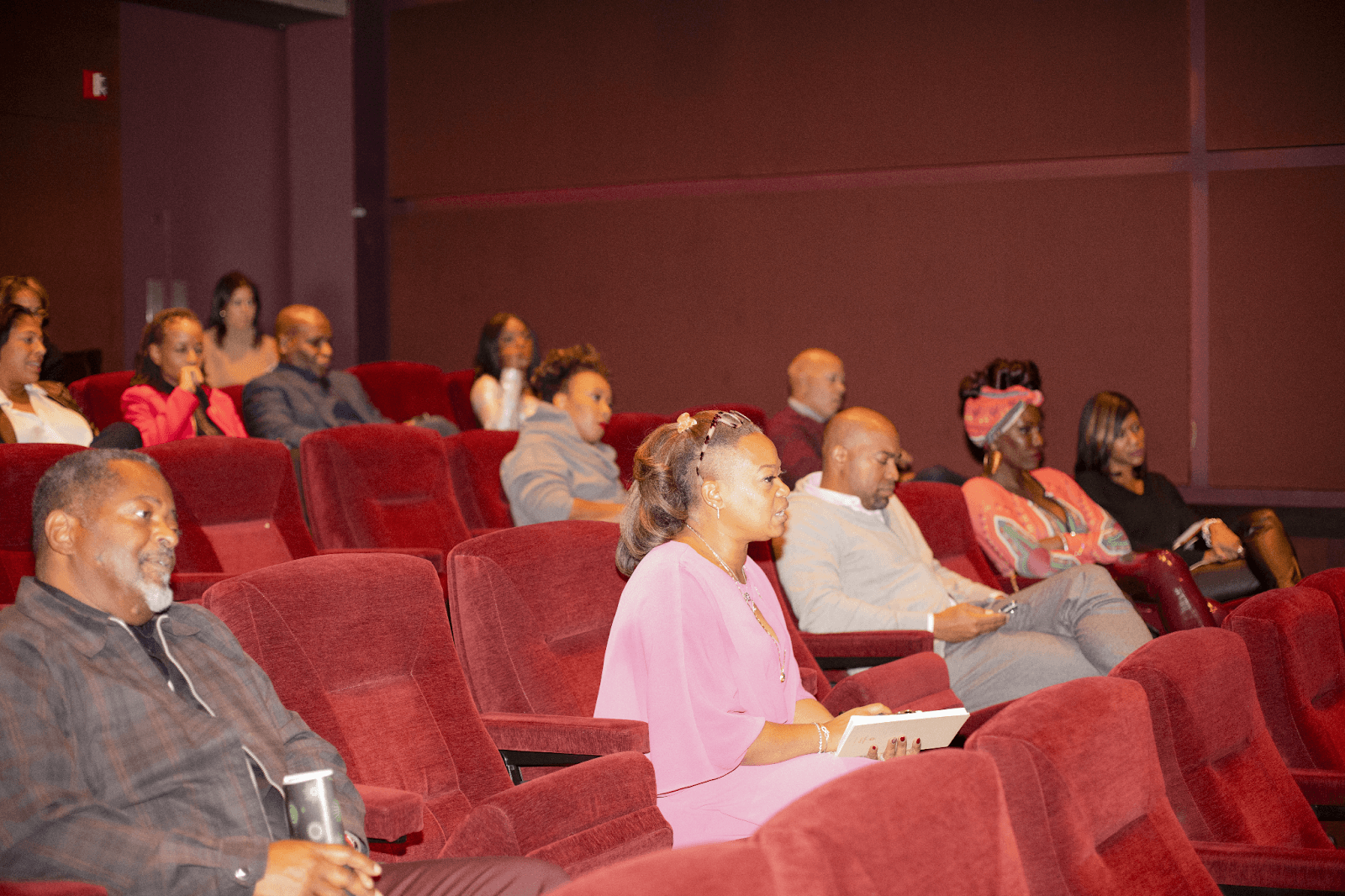 A diverse group of audience members seated in a theater, attentively listening to the discussion, with some taking notes or reflecting on the conversation.