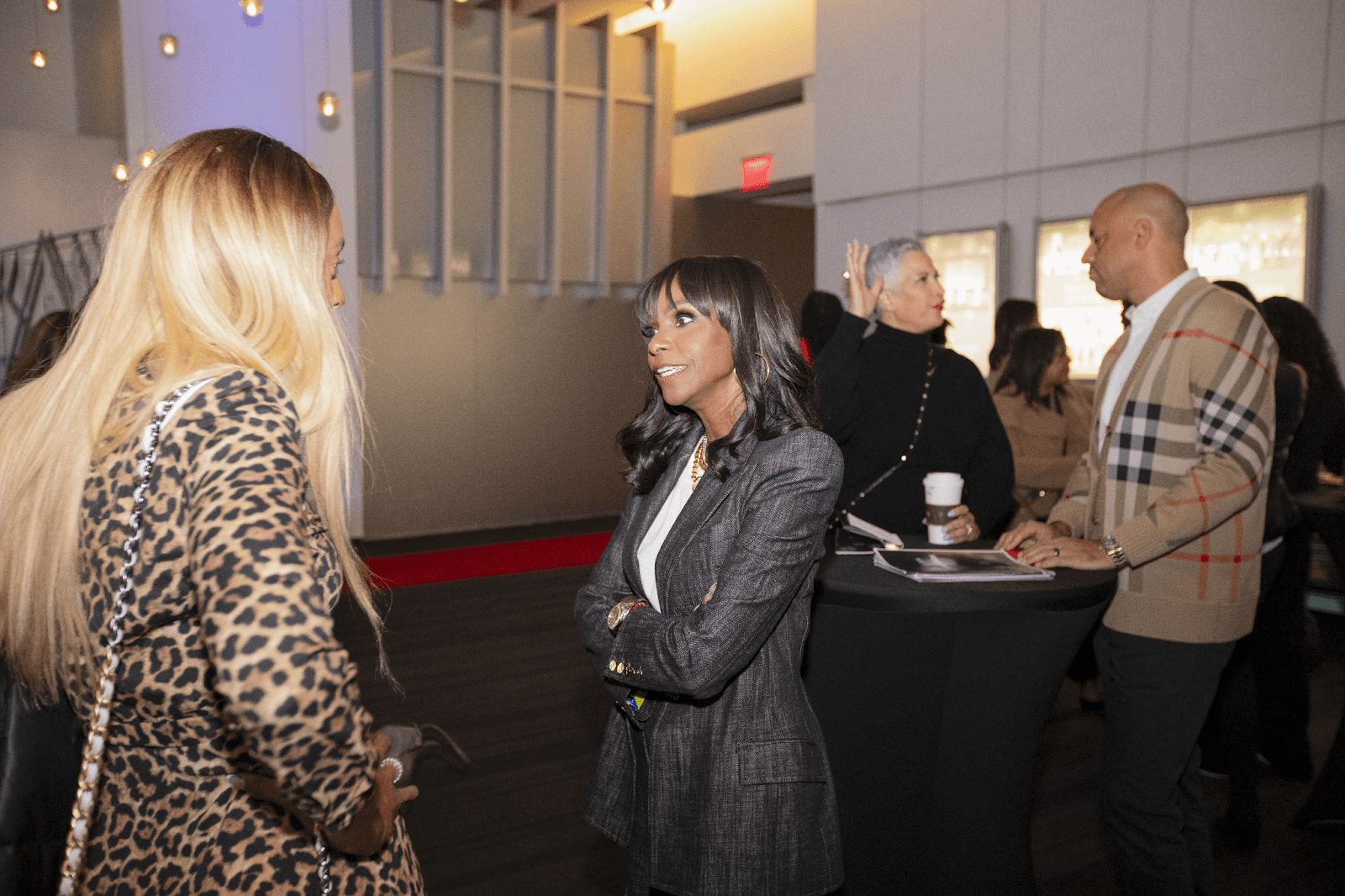 Two women engaged in a conversation at a networking event, with others mingling in the background.