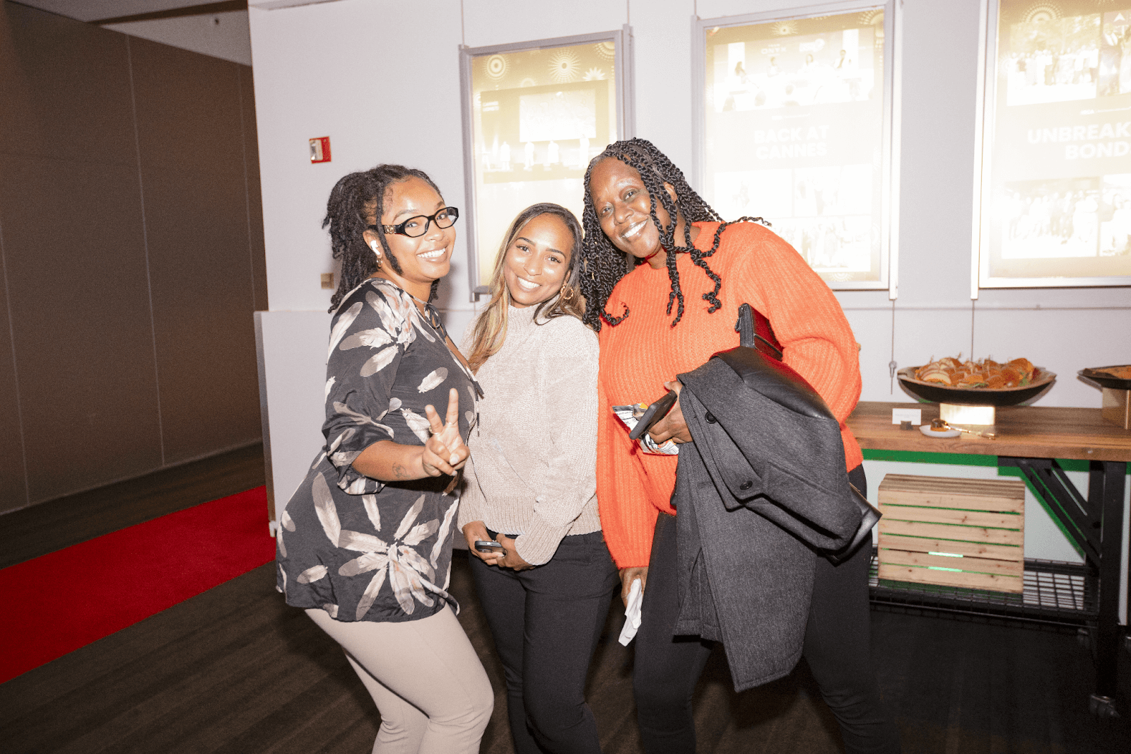 Three women posing happily together, showcasing bright smiles at a casual event.