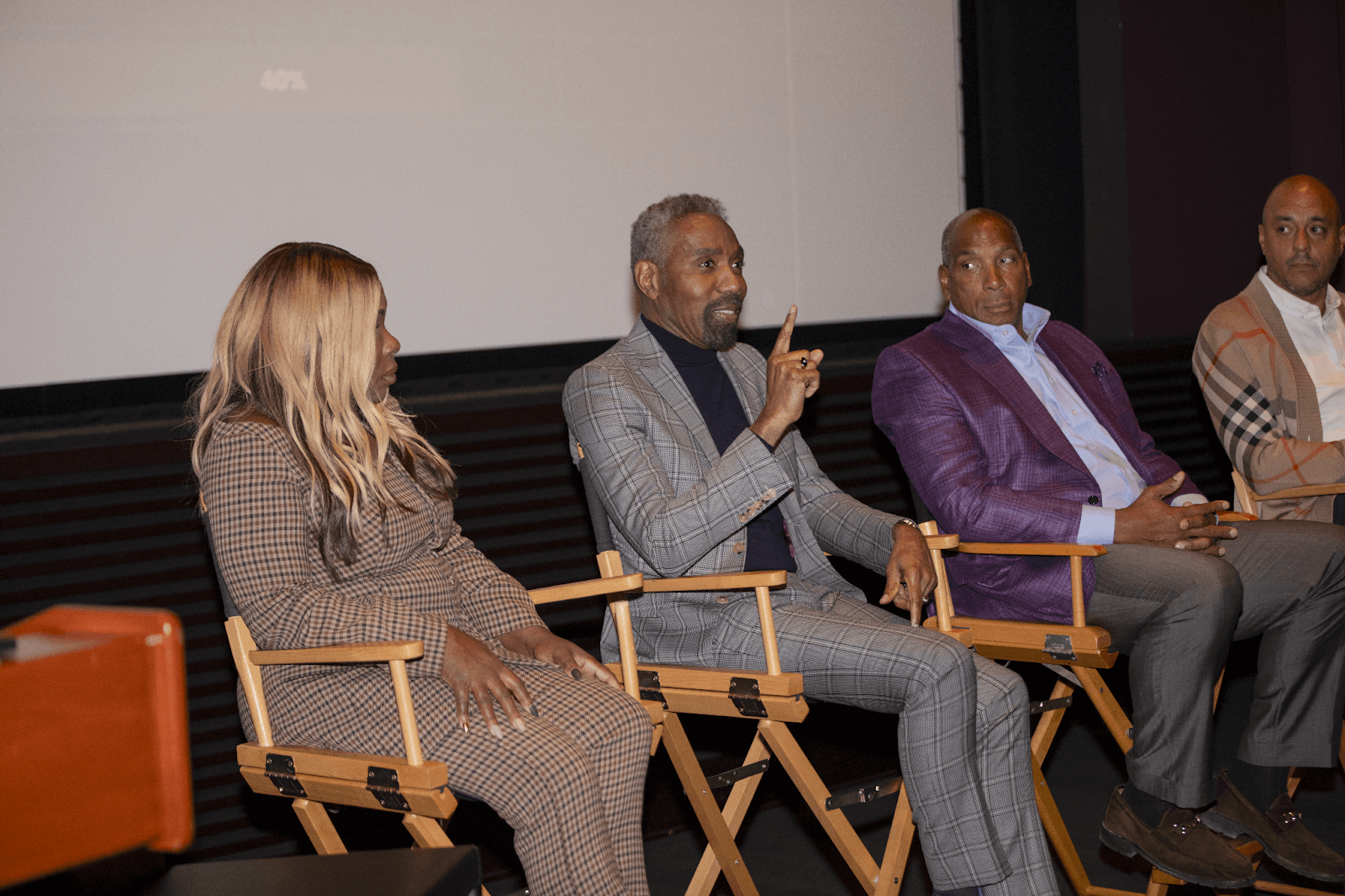 A panelist passionately speaking during a professional discussion, seated alongside other panel members in formal attire, with an audience in view.
