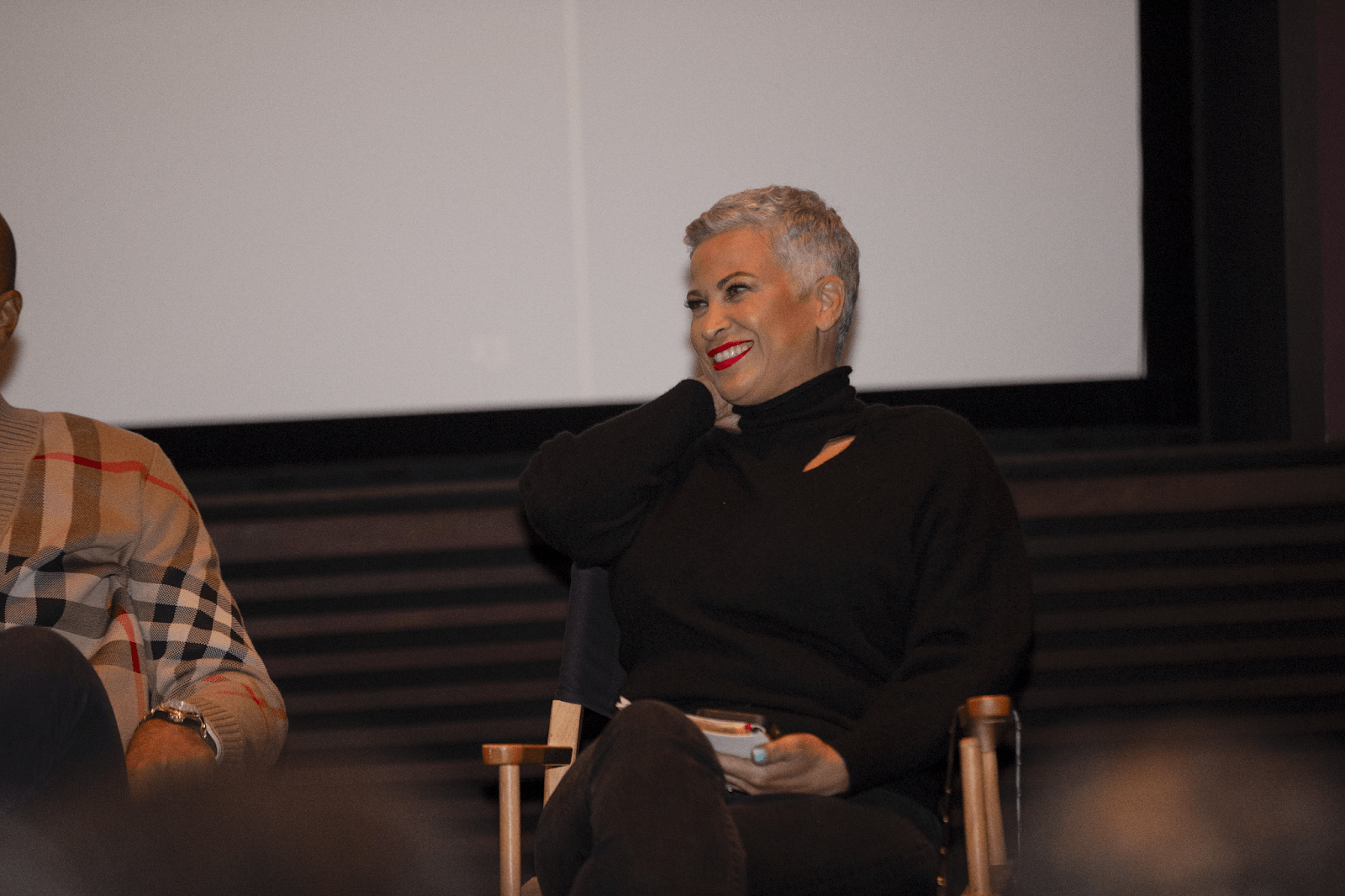 A smiling panelist seated in a director’s chair, relaxed yet engaged in the ongoing conversation.