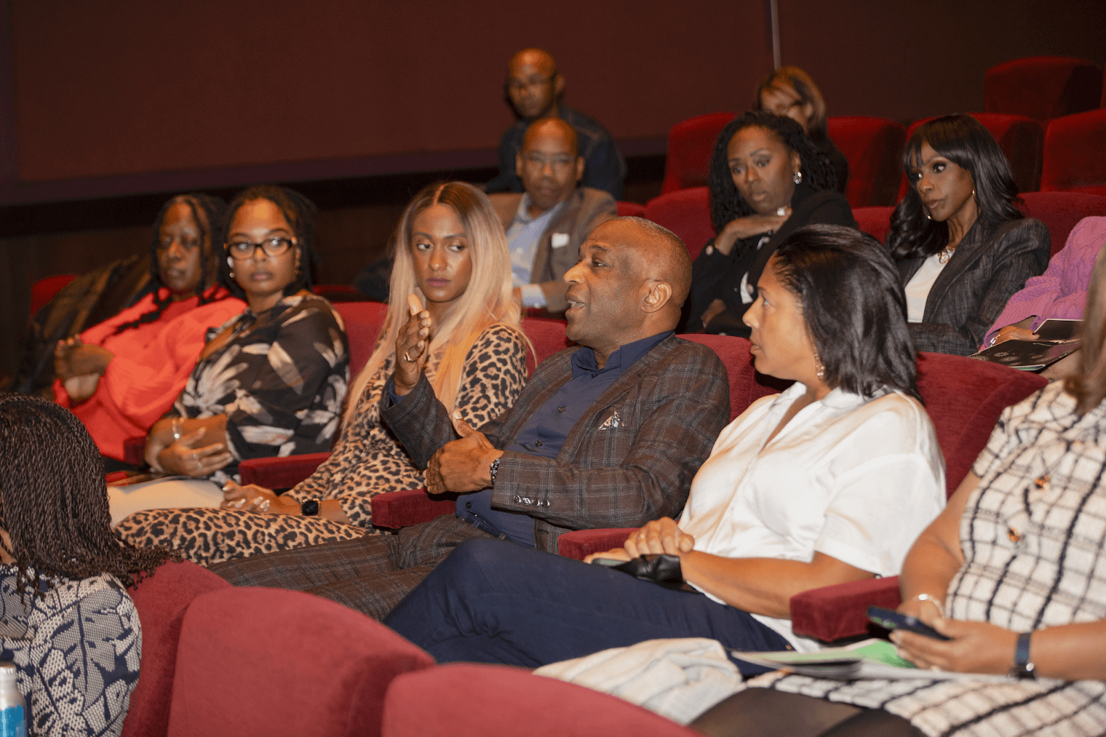 A member of the audience actively participating in the discussion, surrounded by others seated attentively in a theater setting.