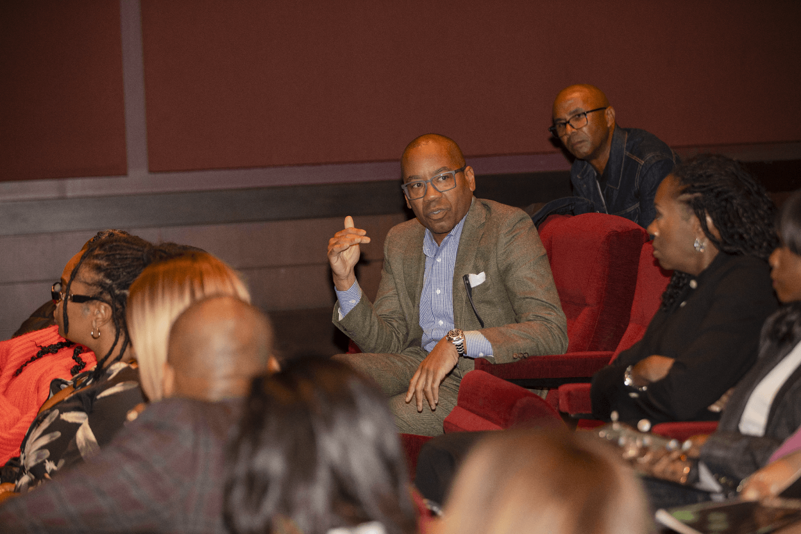 A male audience member speaking with an expressive gesture, while others attentively listen during the event.
