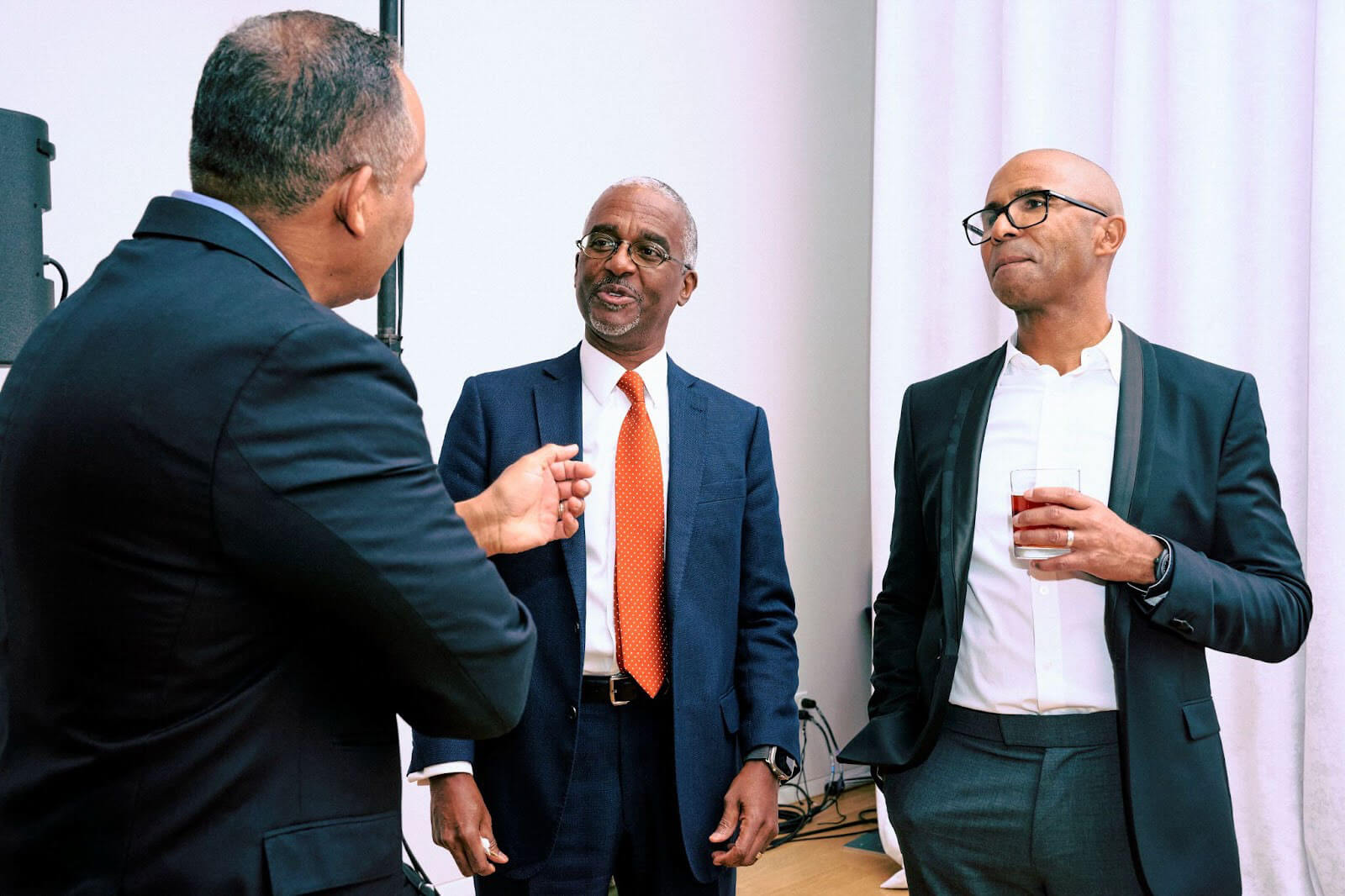 Three men in formal attire engaged in a conversation during the event, one holding a drink.