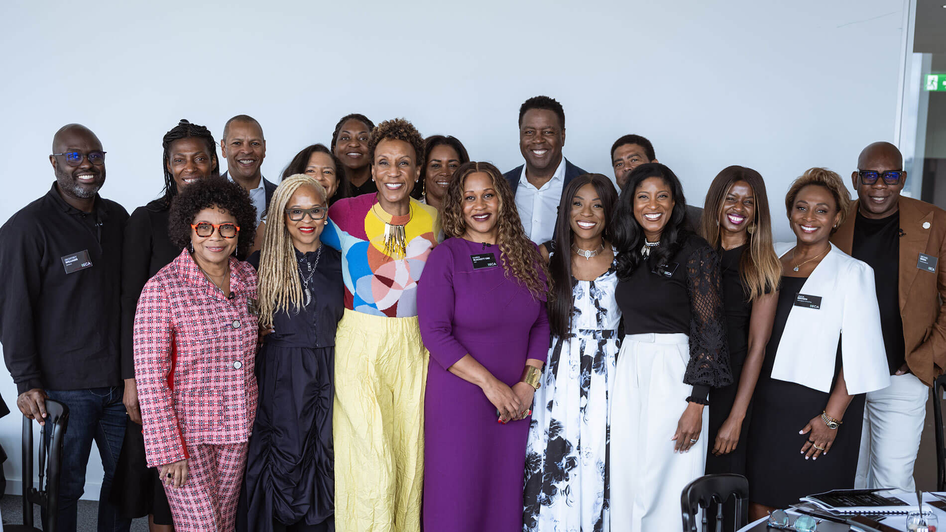 A diverse group of professionals posing together, smiling warmly in a brightly lit conference room. The attendees are dressed in vibrant and formal attire, showcasing camaraderie.