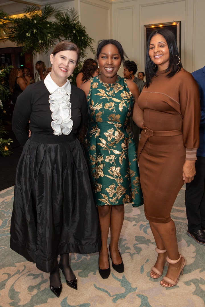 Three women dressed in formal gala attire, smiling and posing together for a photo at a gala event.