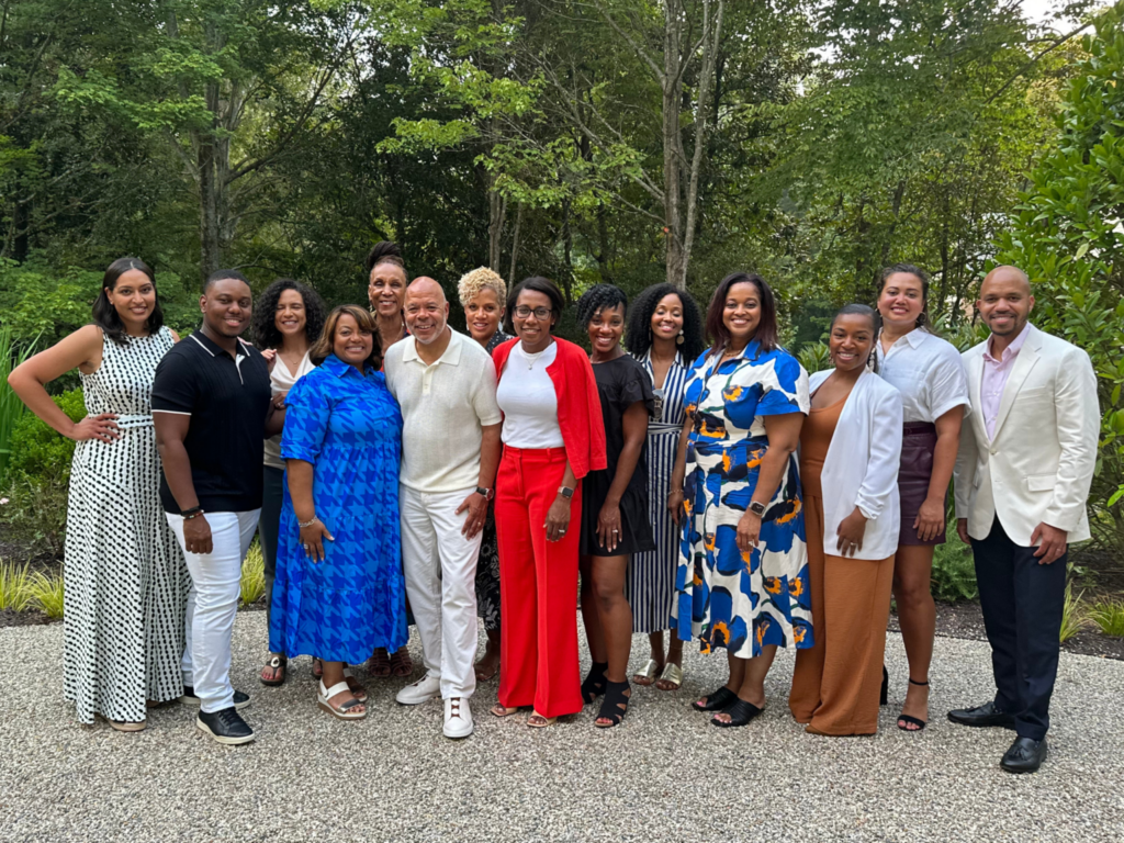 A large group of people in colorful outfits gathers outdoors, smiling for a group photo.