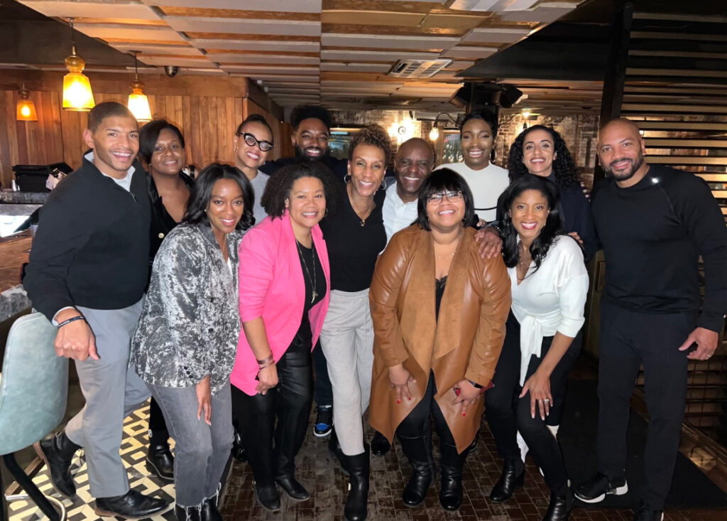 A dozen friends or colleagues gathered in a warmly lit venue, smiling together for a group shot.