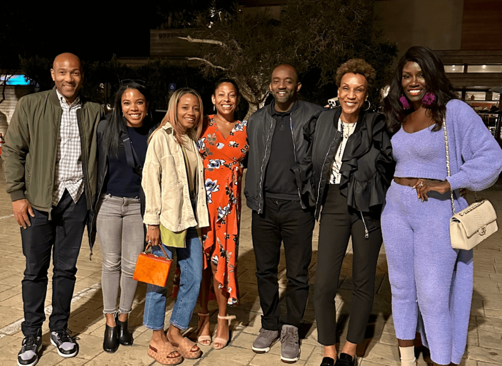 Seven people in casual-chic attire smiling for a group photo at night.