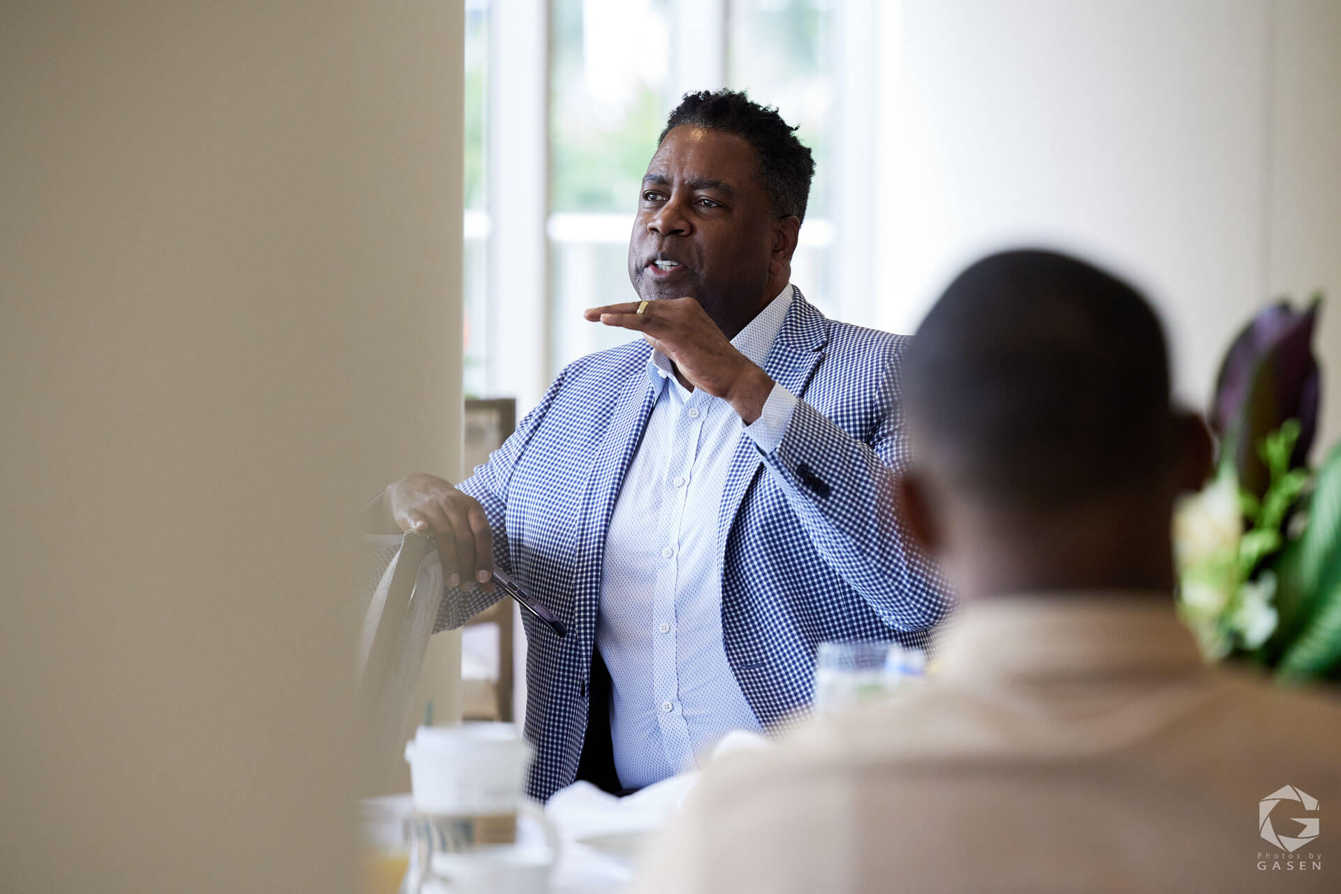 A man in a checkered blazer gesturing expressively while speaking in a professional setting.