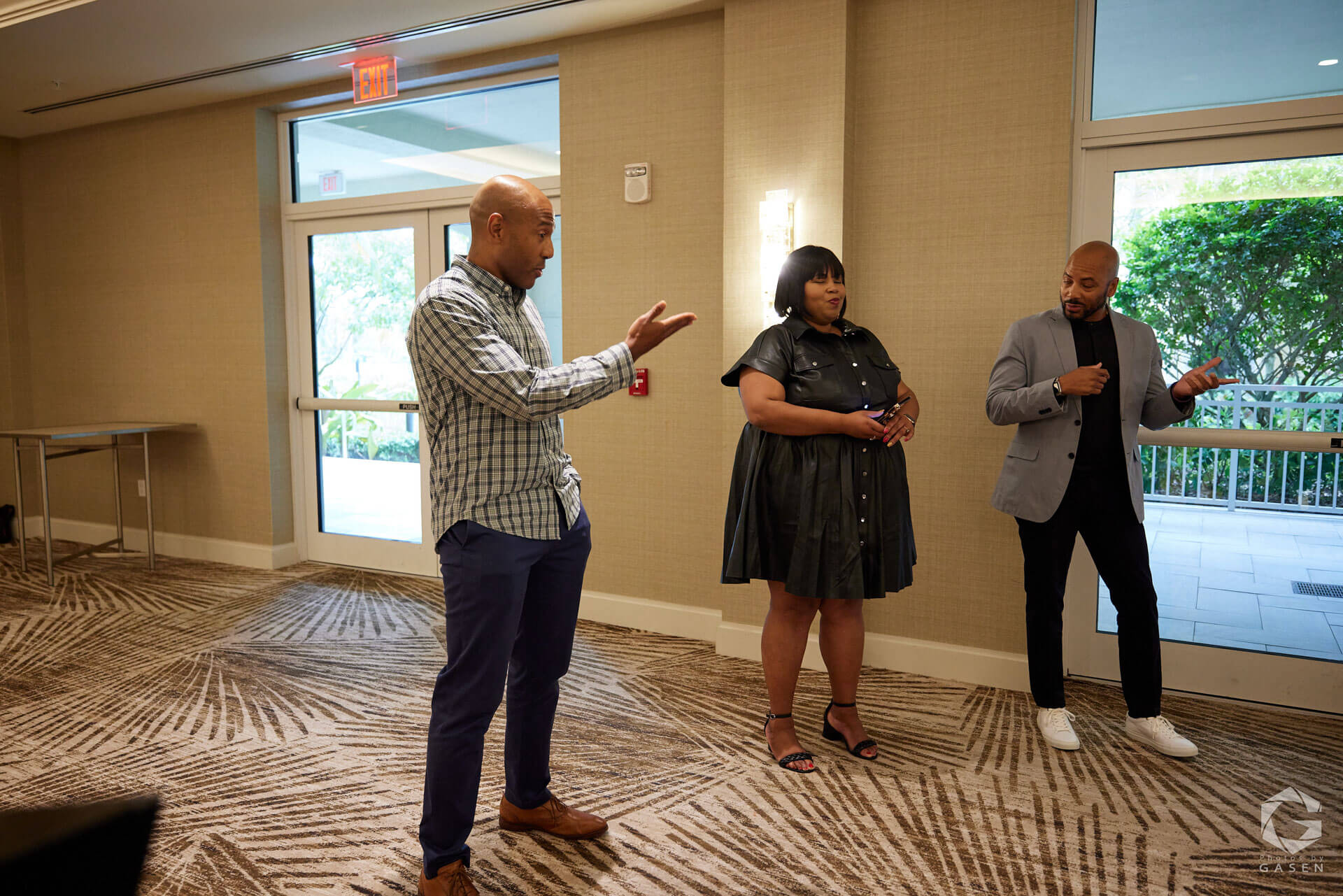 Three individuals standing in front of a window, actively engaged in conversation during a professional meeting.
