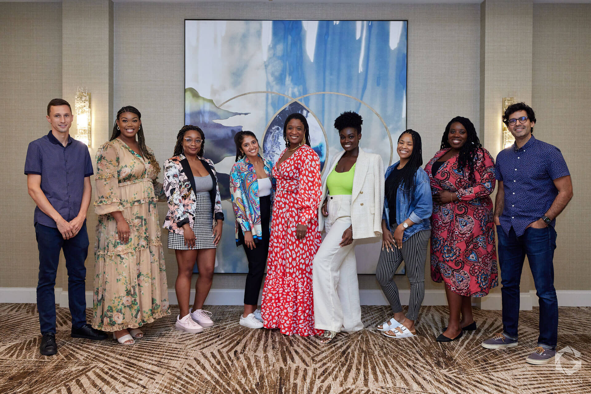 A diverse group of eight people posing for a photo against an abstract backdrop, showcasing a vibrant and celebratory atmosphere.