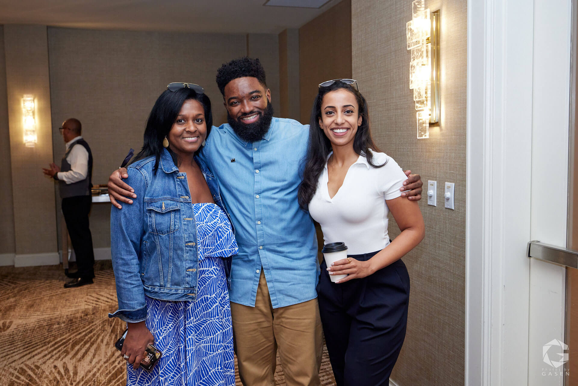 Three individuals smiling and standing closely together, creating a warm and friendly vibe at an indoor event.