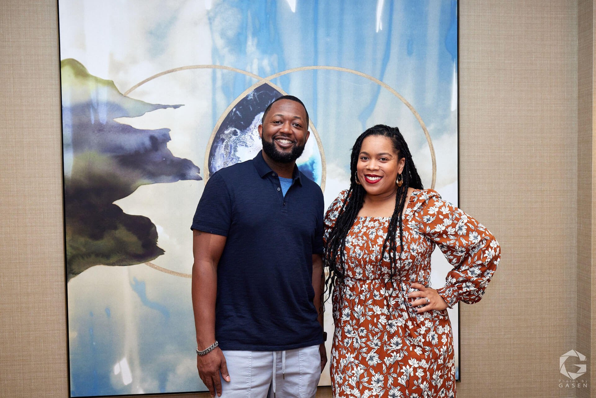 A man and a woman posing for a photo against a vibrant art backdrop, both smiling warmly.