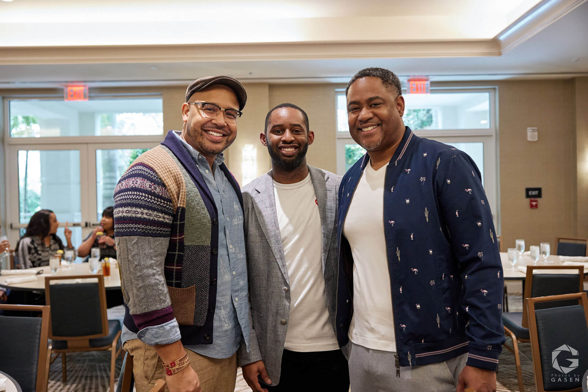 Three men smiling broadly, standing close together, and posing for a photo in a casual yet professional atmosphere.