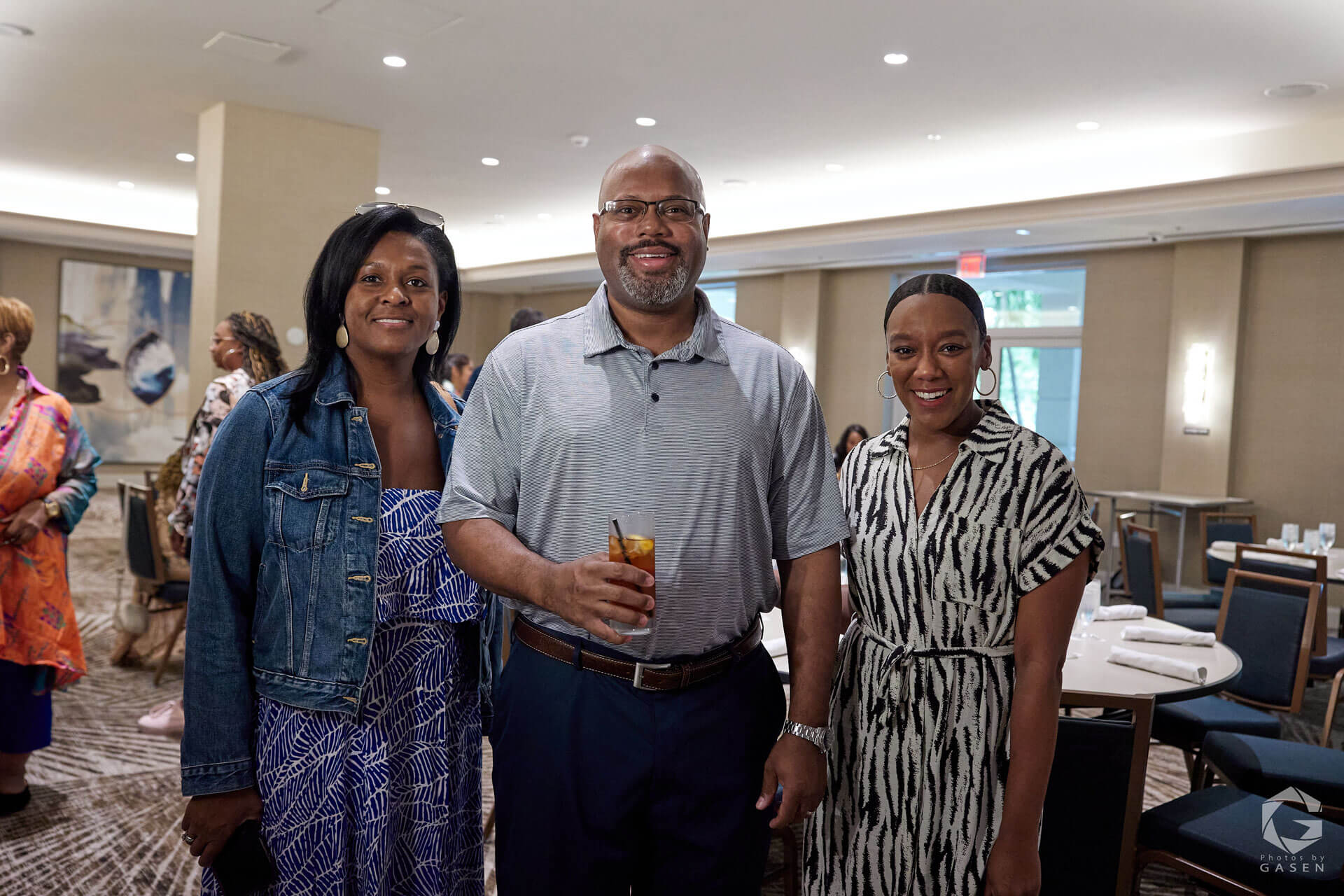 Two women and a man standing together, smiling for the camera, with a drink in hand, during a networking event.