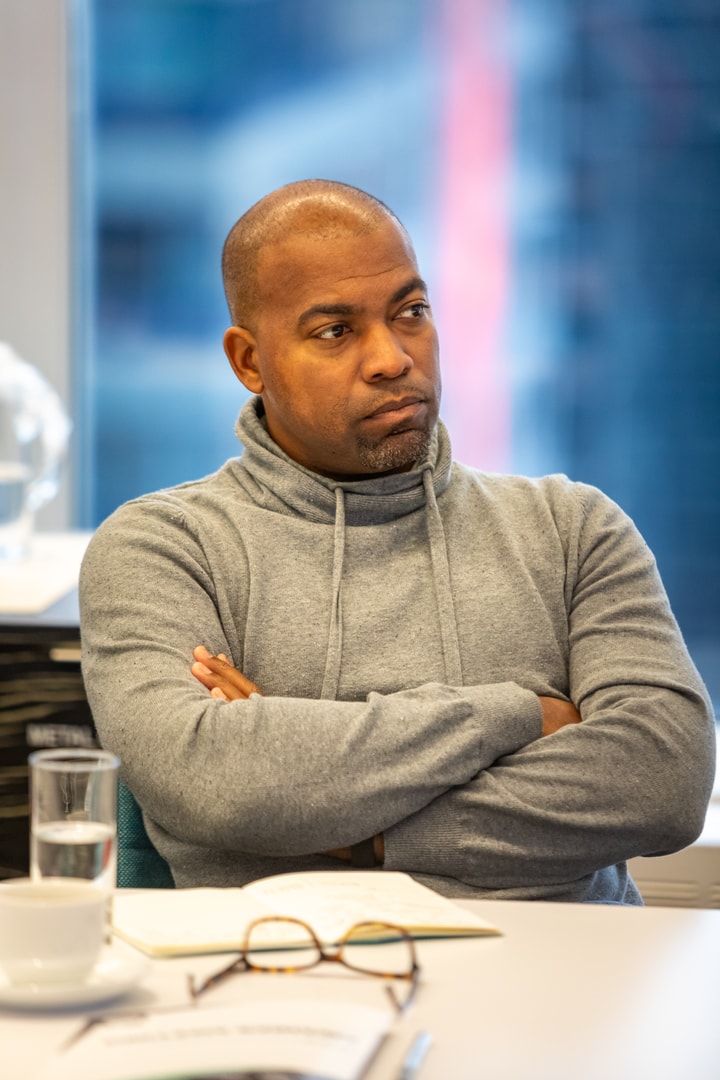 Man in gray hoodie with arms crossed at a conference table.