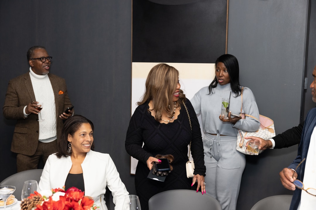 A group of elegantly dressed individuals engages in conversation at an upscale gathering, holding drinks and sharing smiles.