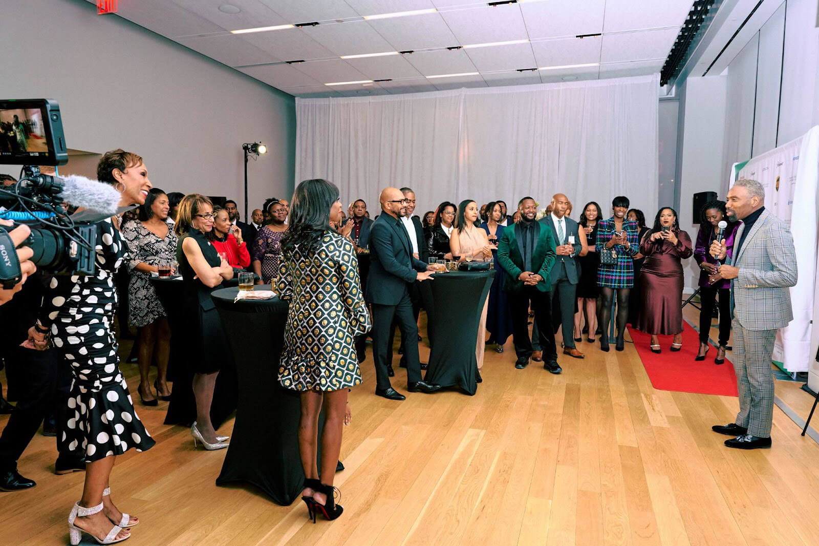 A speaker addressing a room of attendees during a formal gathering, with guests standing and engaged.