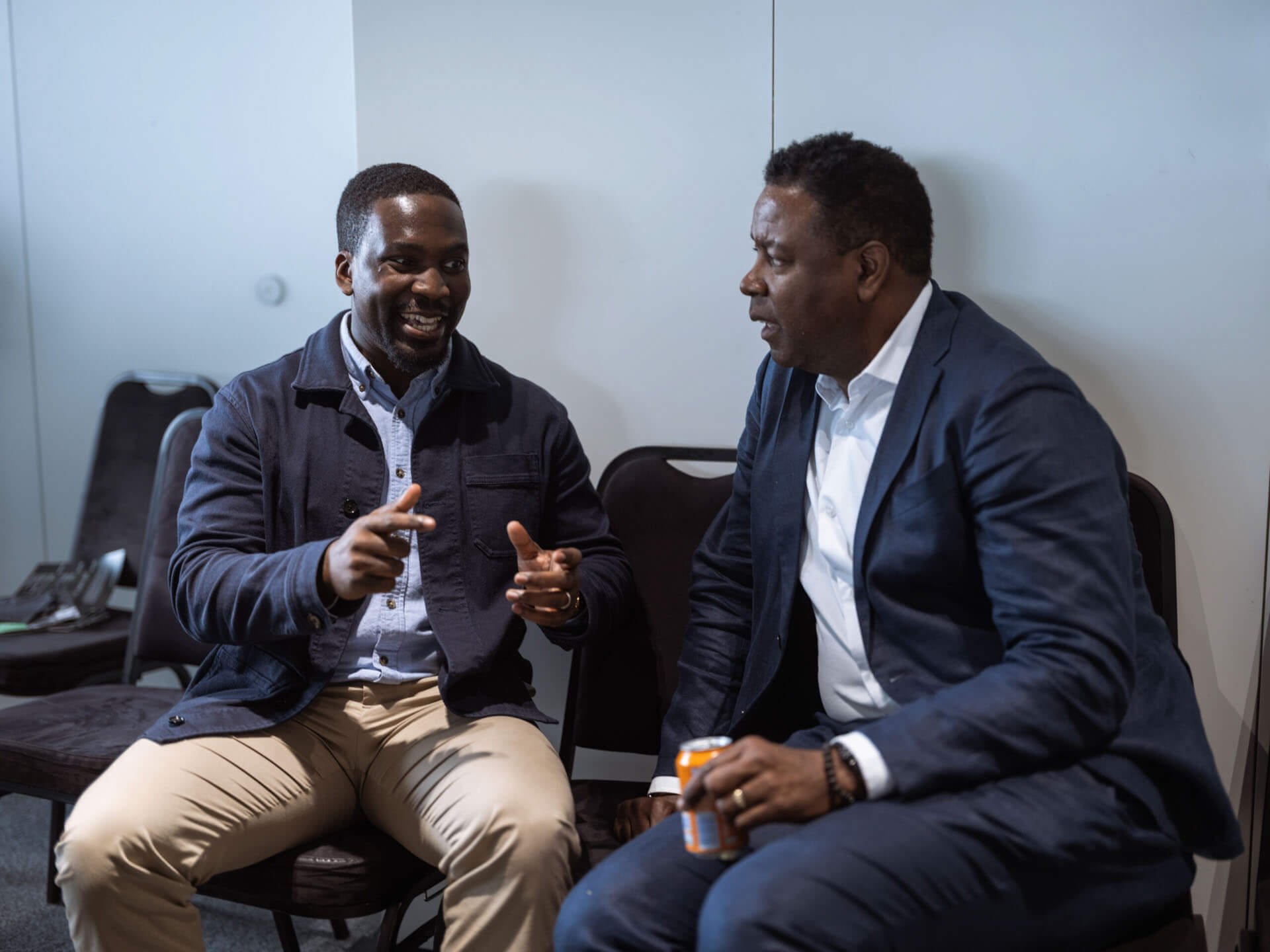 Two men seated, sharing a casual conversation during a break at an event.