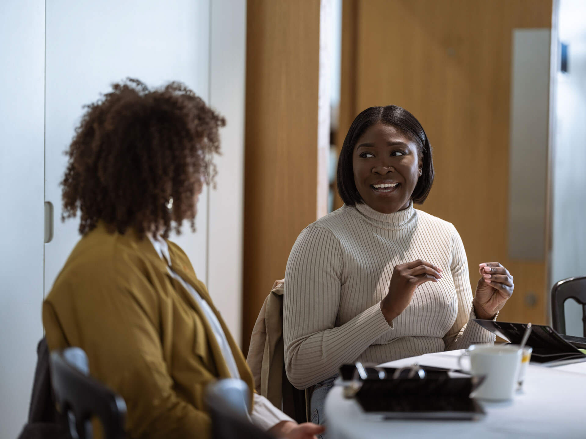 Two women seated at a table, engaged in an animated conversation during a workshop or meeting.