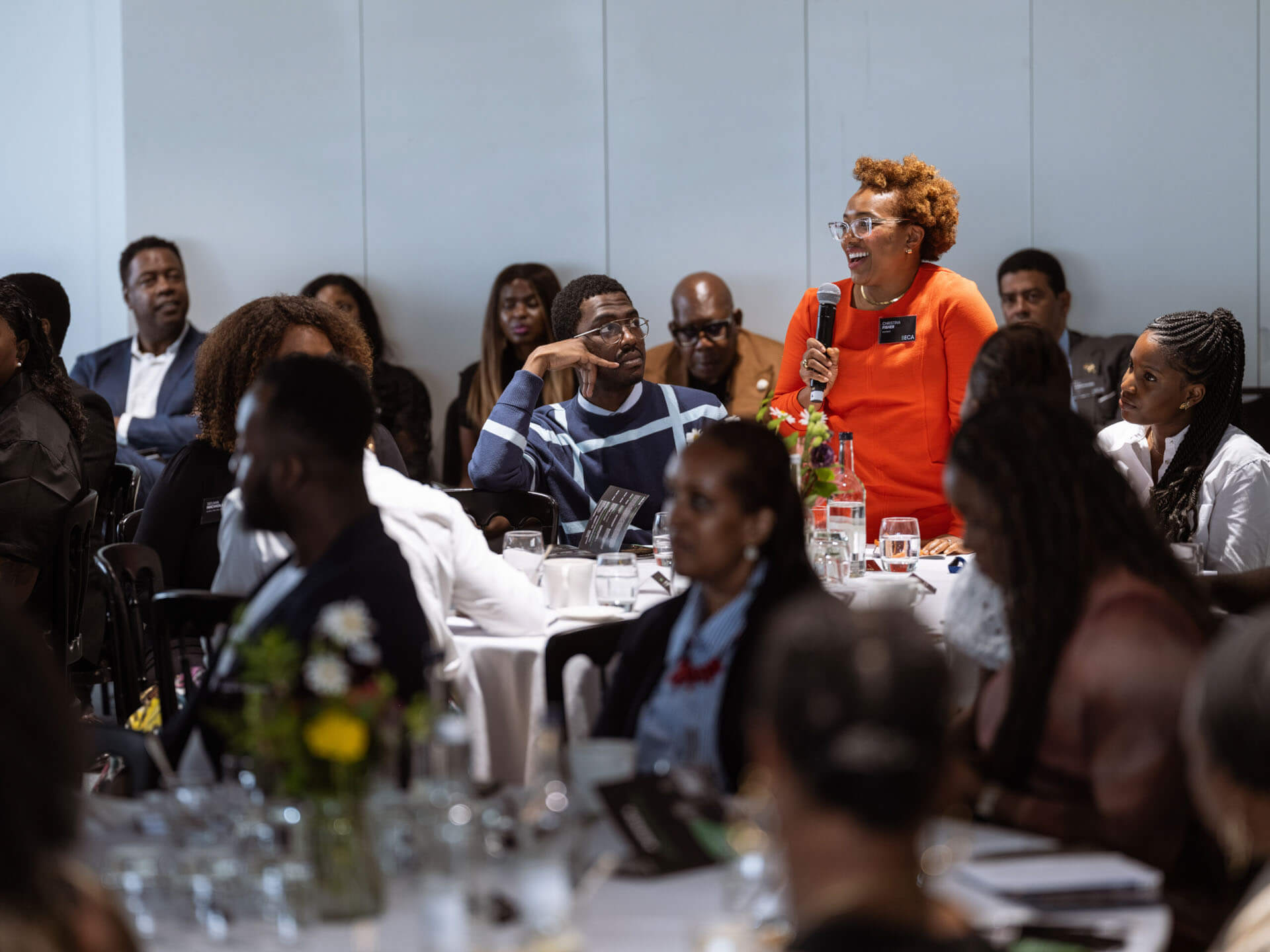 An audience member in bright orange attire speaking with a microphone during a session.