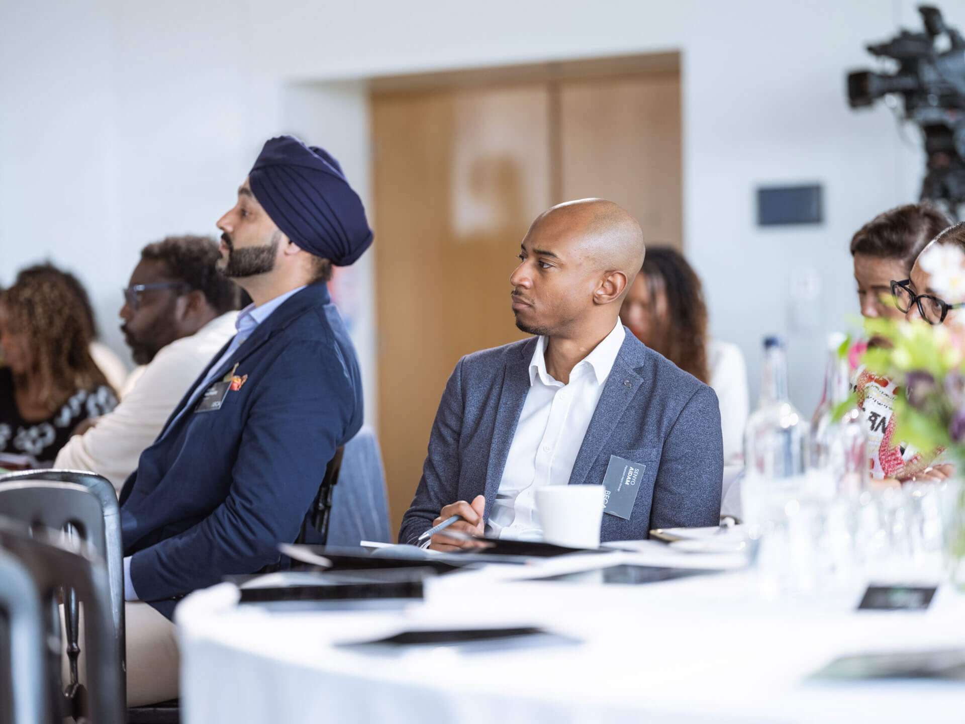 Attendees sitting at a round table, attentively listening during a professional event.