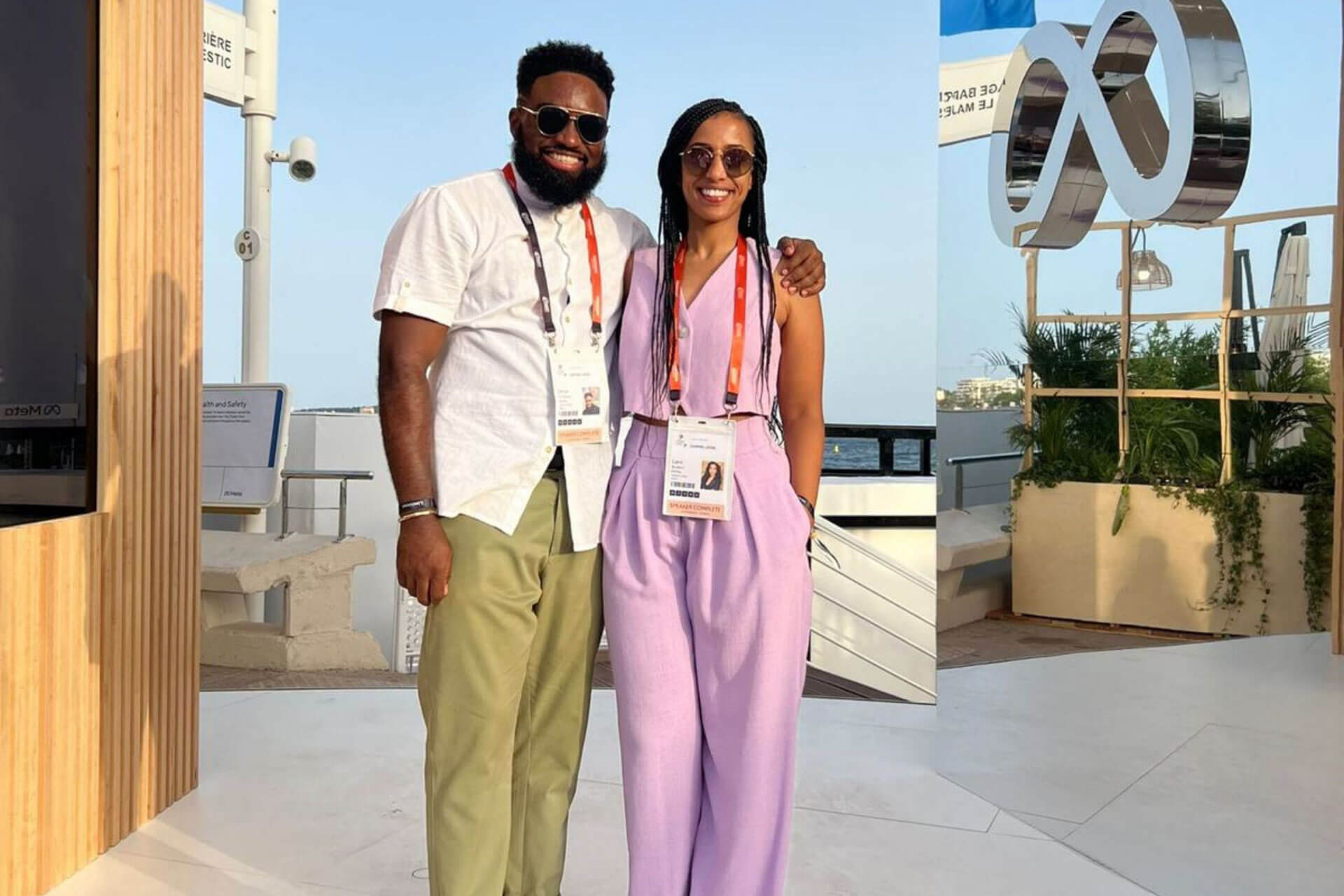 A man and woman posing together at a Meta event, wearing event badges and standing in a sunny outdoor space.