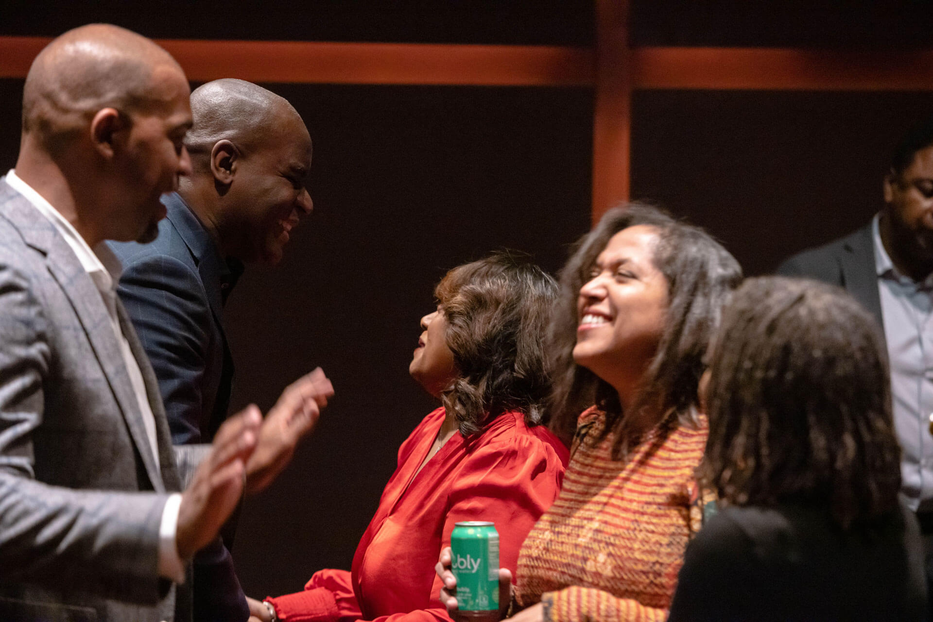 A group of individuals engaging in animated conversation and laughter in a theater setting.