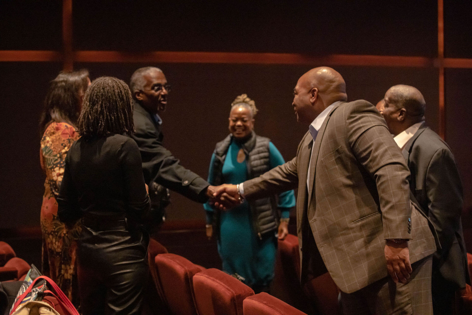 A group of people standing in a theater, shaking hands and exchanging pleasantries.
