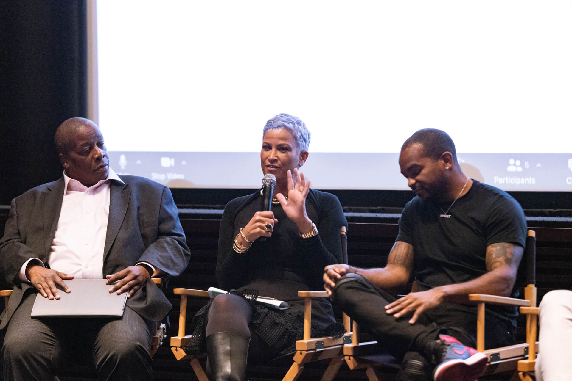 A panelist with short gray hair speaking into a microphone, seated between two other participants in a professional setting.