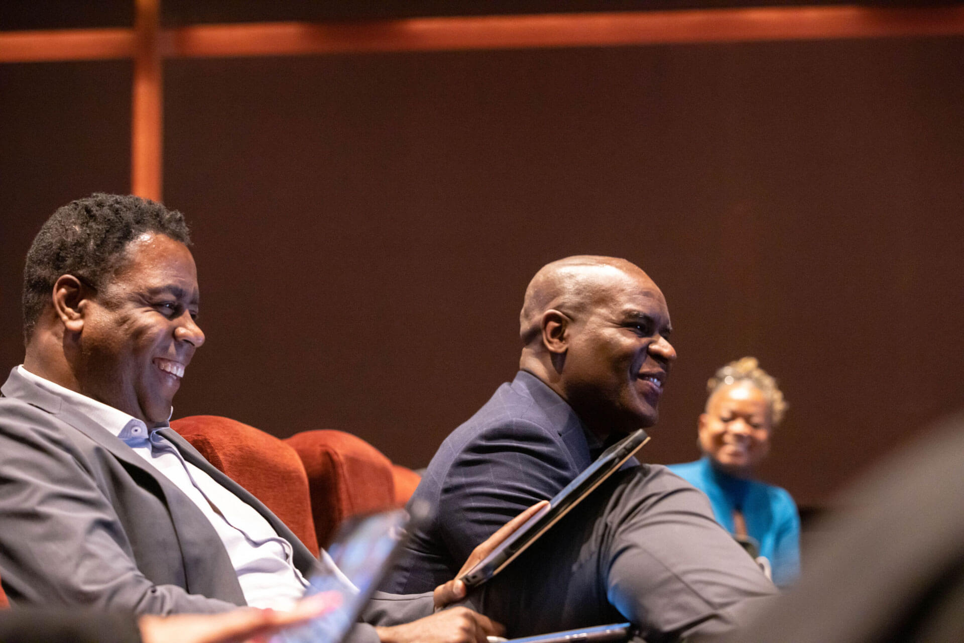 Two men seated in a theater audience, smiling and enjoying the discussion.