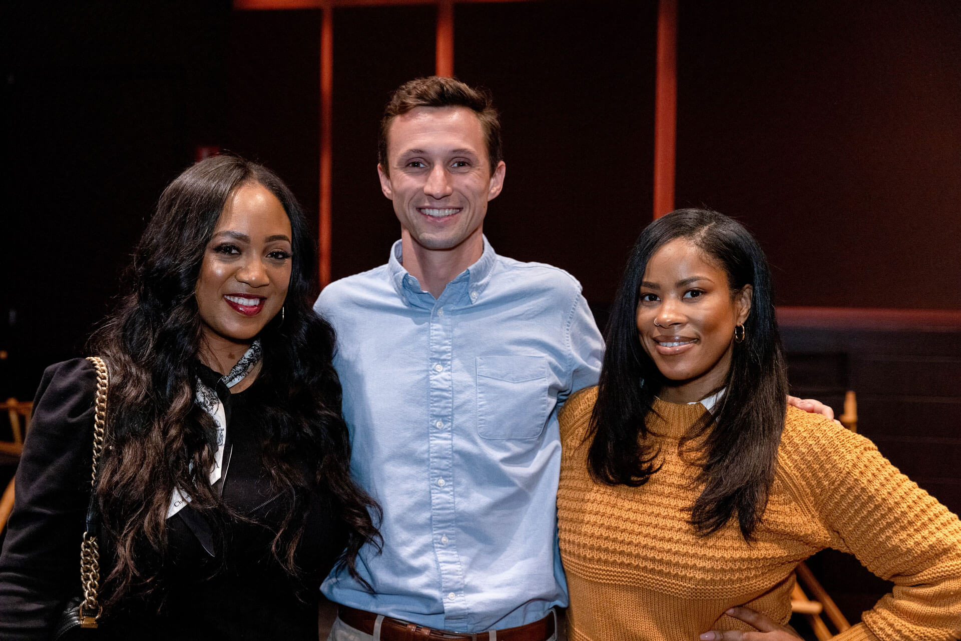 A group of three colleagues or friends, two women and one man, smile together for a photo in a professional but relaxed environment.