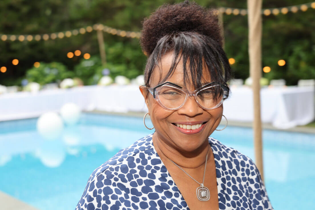A woman in a blue-and-white patterned outfit, smiling near a pool decorated for an outdoor event.