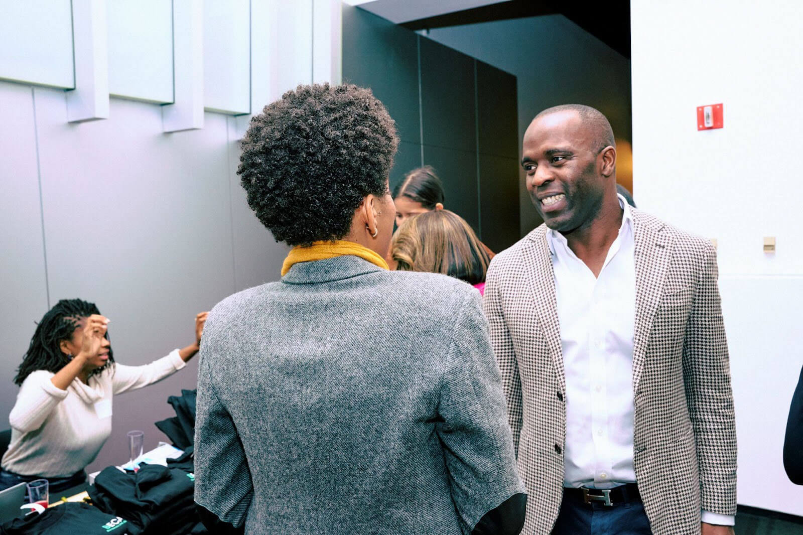 A man and a woman in conversation at a professional event, exchanging smiles as others interact in the background.