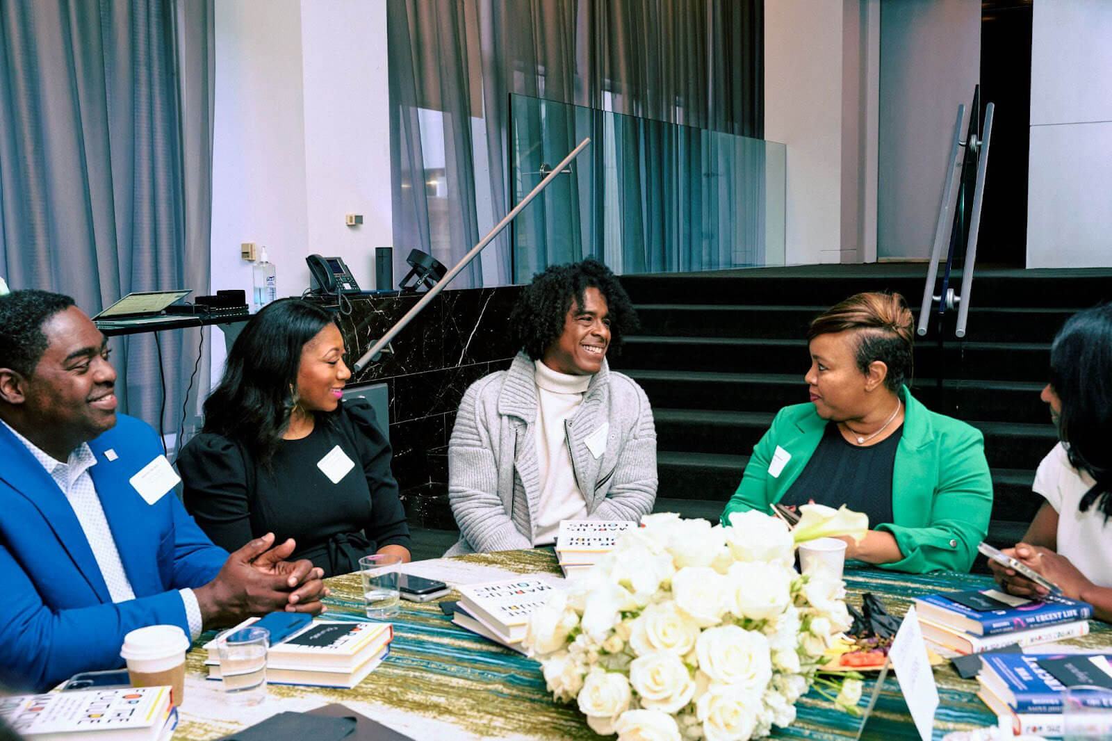 A roundtable discussion among a group of attendees, sharing insights and ideas, with books and coffee cups spread across the table.