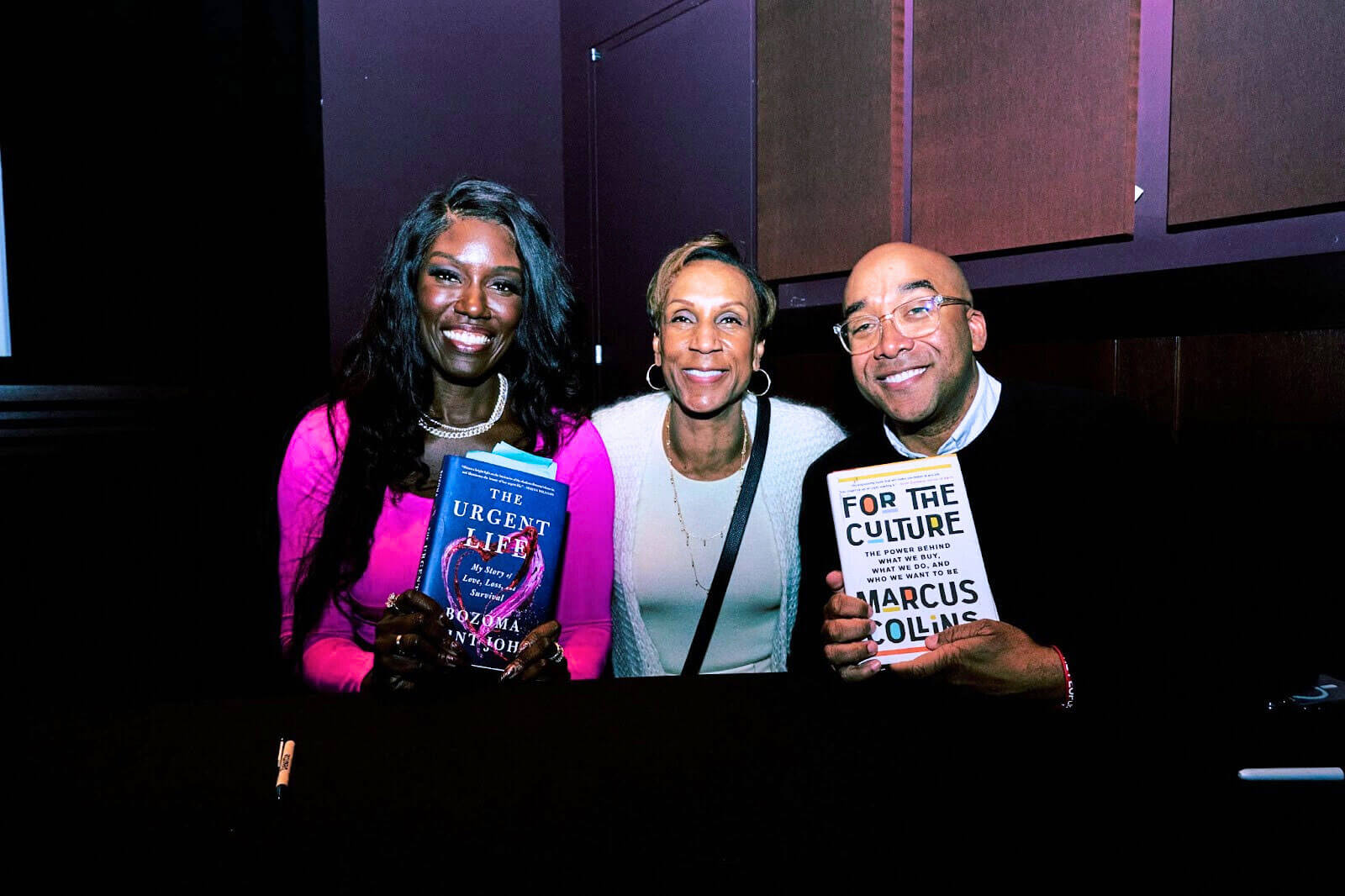 Three individuals posing with books, smiling broadly at a book signing or celebratory event.