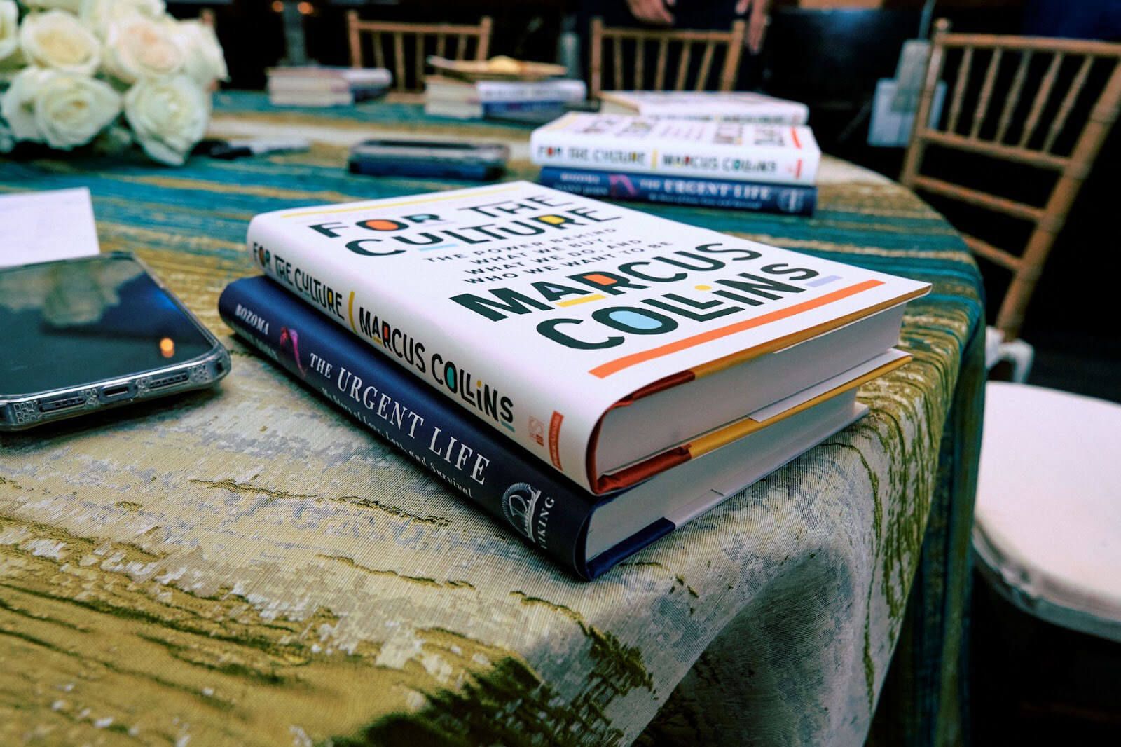 A table featuring a stack of books, including "For the Culture" by Marcus Collins and "The Urgent Life" by Bozoma Saint John, alongside a smartphone.