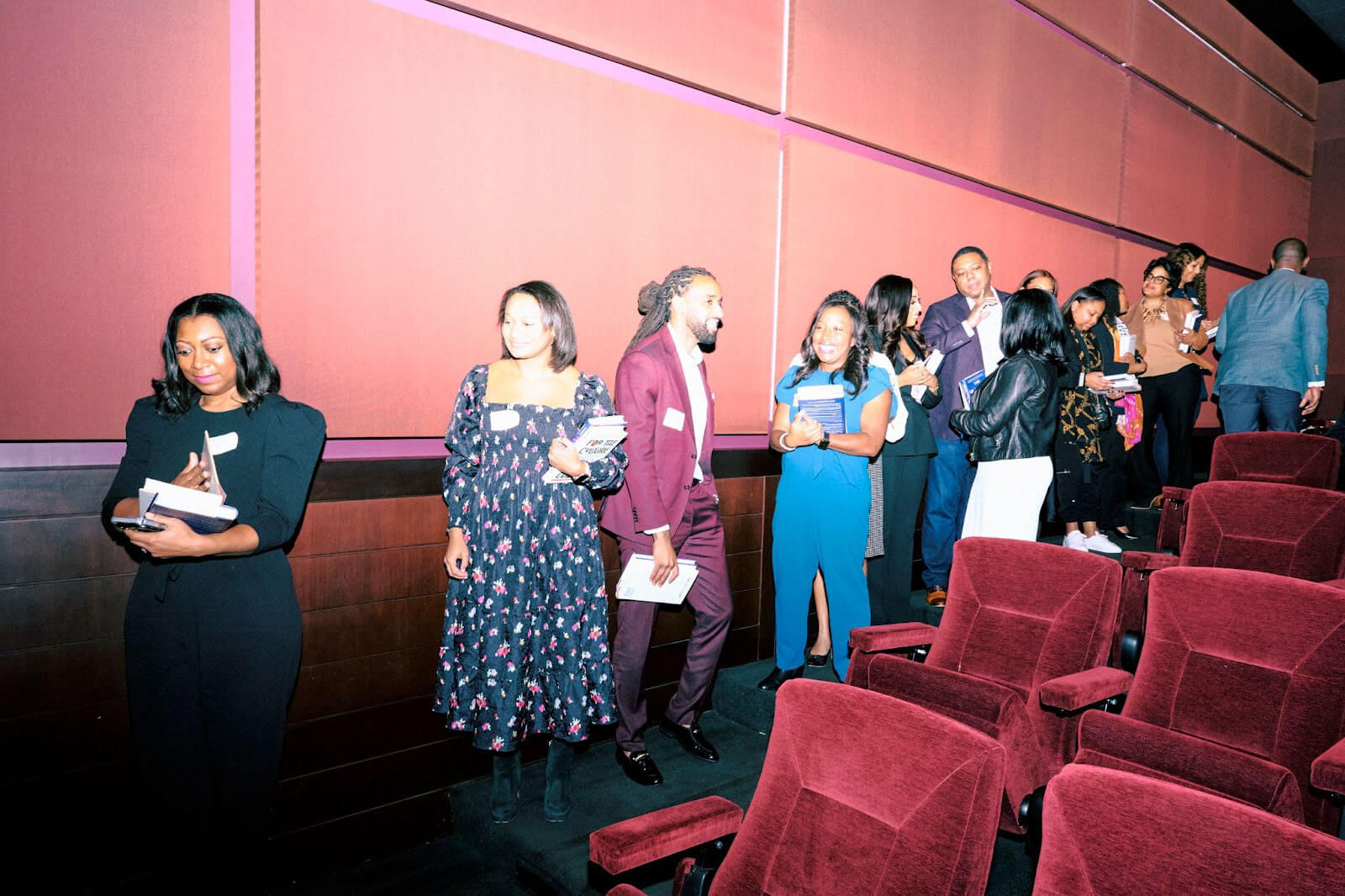 A line of attendees in a theater holding books, engaged in a signing or networking event.