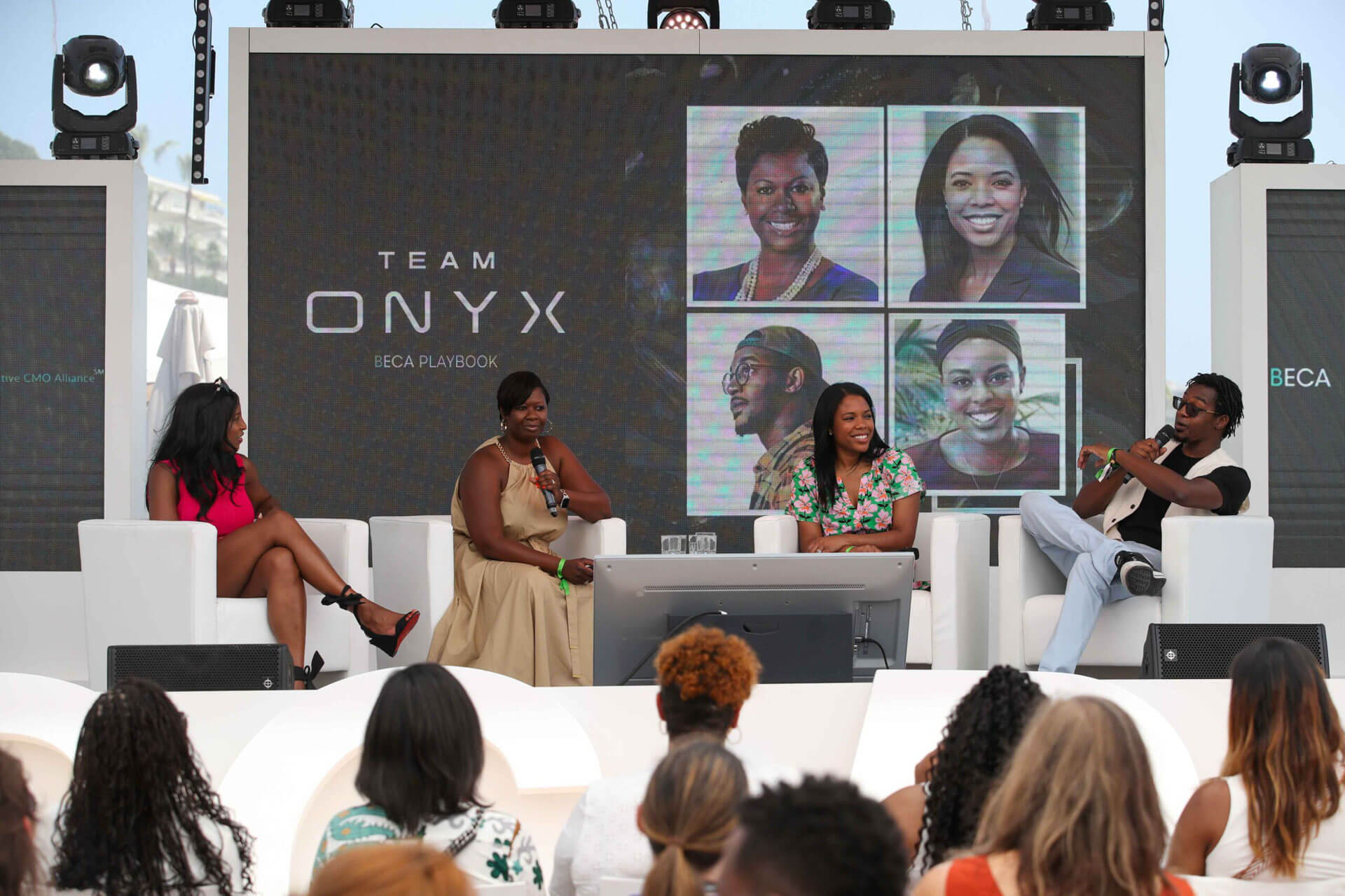 Four panelists seated on stage in a discussion, with "Team Onyx" and photos displayed on the large screen in the background.
