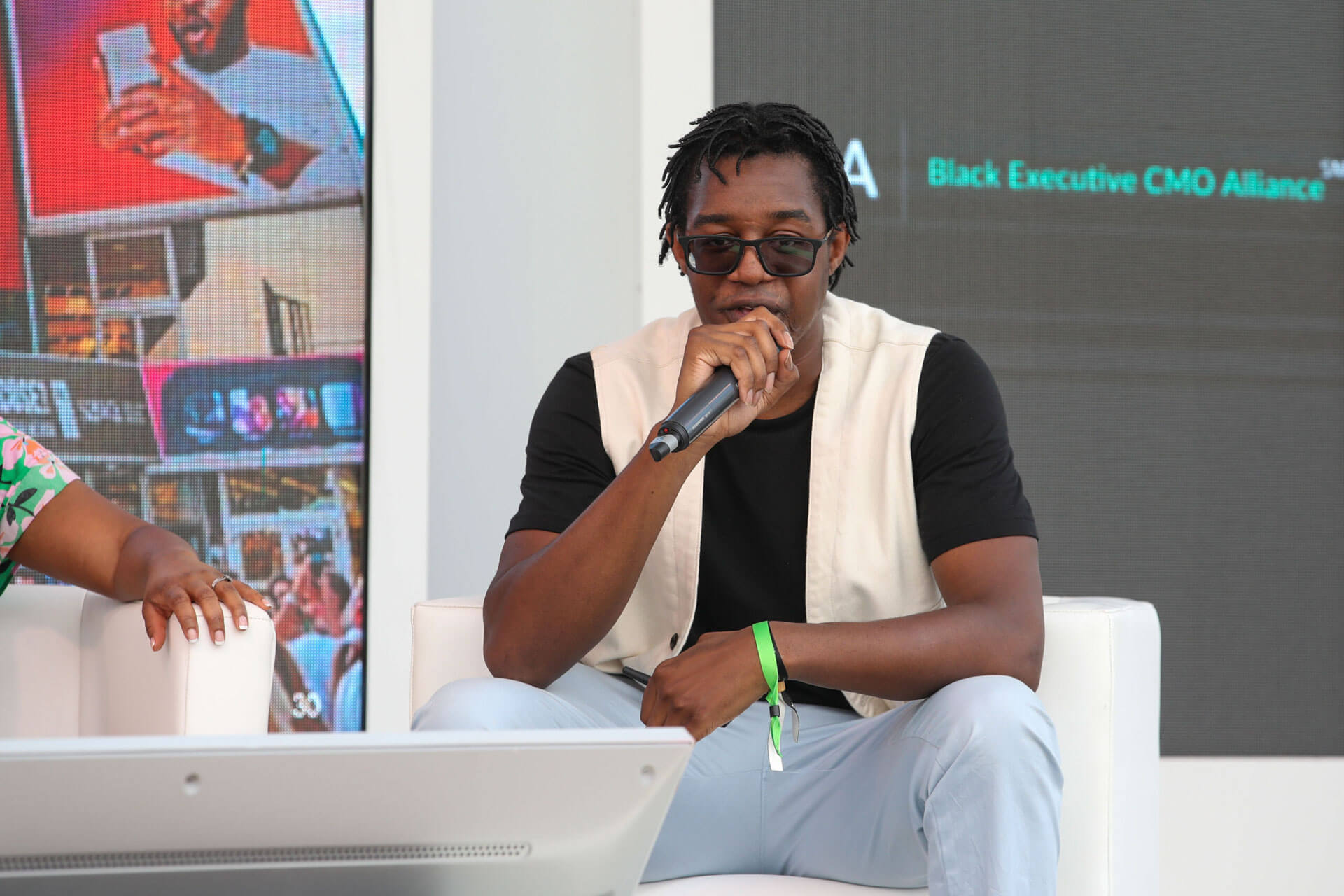 A male panelist in a black shirt and light vest, speaking into a microphone during the discussion.